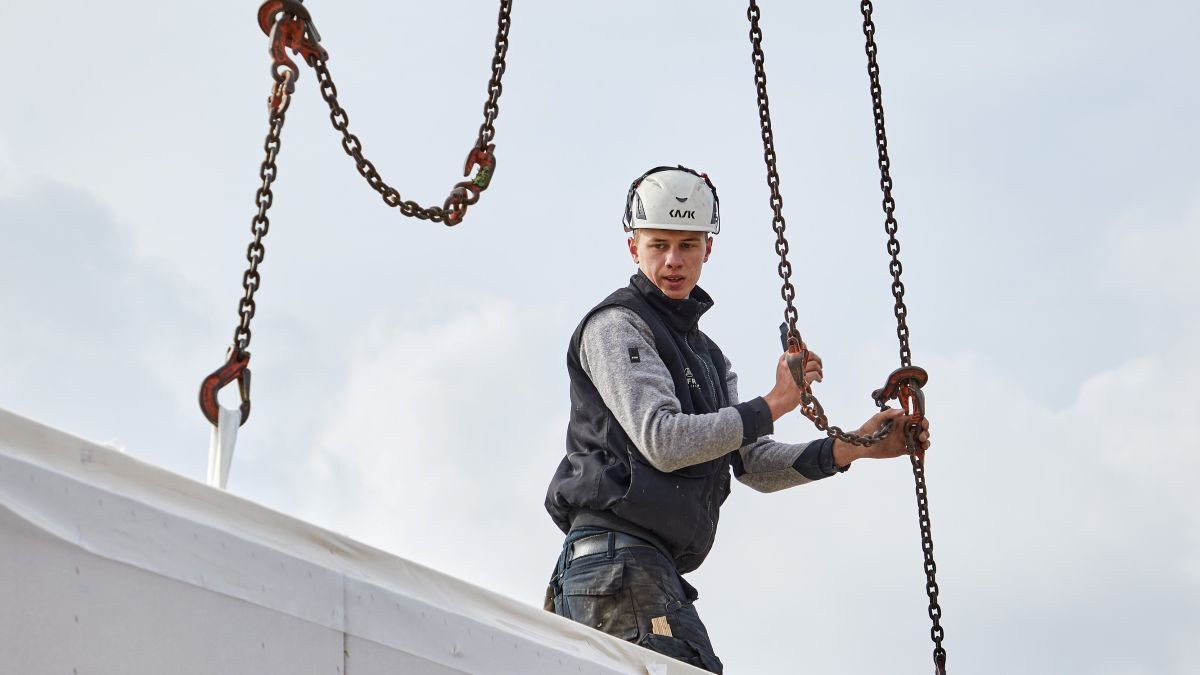 Bissantz realisiert bei Baufritz ein Planungsprojekt mit Hebelwirkung zur Steuerung der komplexen Kosten - Das Bild zeigt einen Bauarbeiter, der an einer Kette ein größeres Bauteil zu einem Fertigteil ablässt.